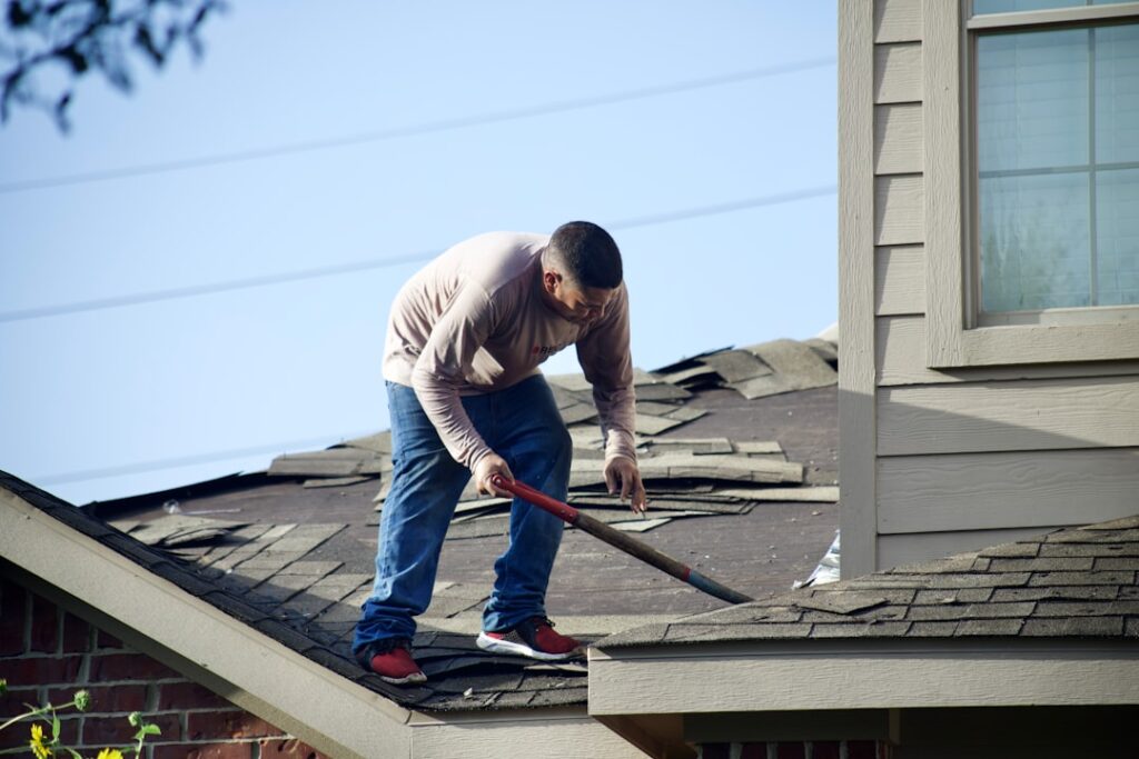 A homeowner gently sweeping leaves and pine needles off a shingle roof with a soft-bristle broom.