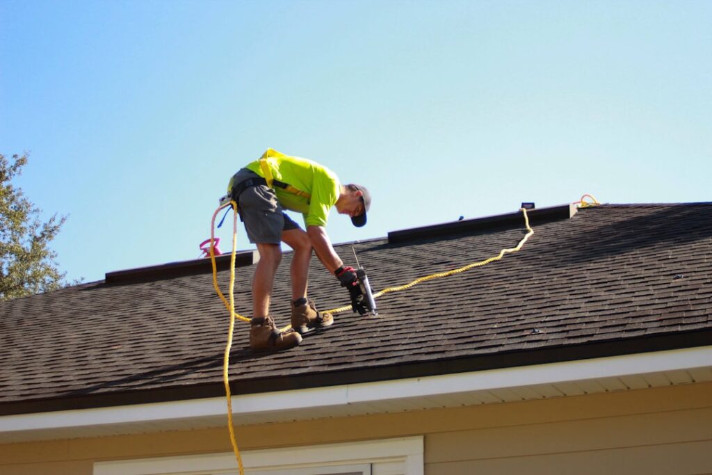 A person using binoculars to inspect an asphalt shingle roof after a storm, with damaged shingles visible.