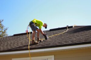 A person using binoculars to inspect an asphalt shingle roof after a storm, with damaged shingles visible.