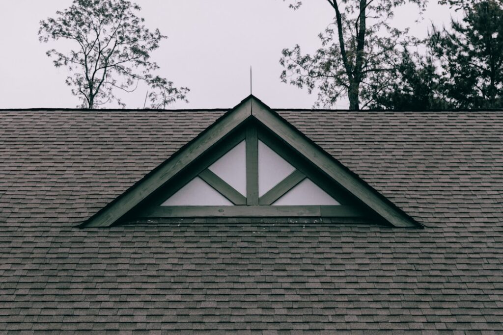 Homeowner inspecting roof shingles from the ground with binoculars beside a suburban house.