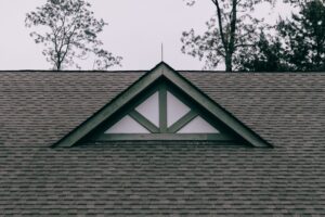 Homeowner inspecting roof shingles from the ground with binoculars beside a suburban house.