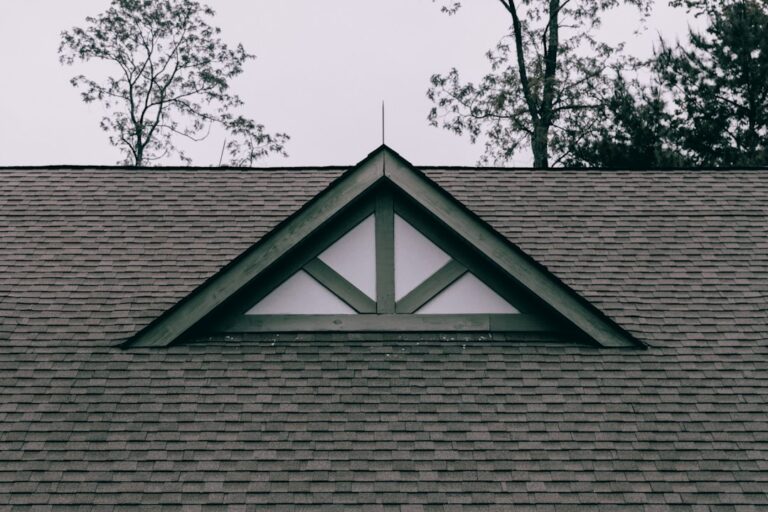 Homeowner inspecting roof shingles from the ground with binoculars beside a suburban house.